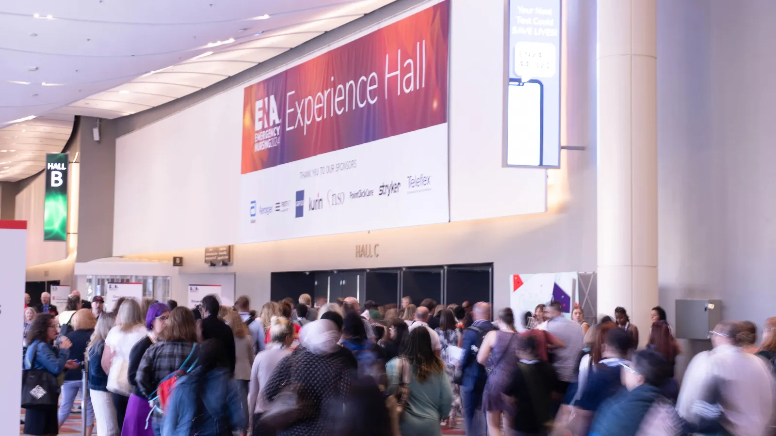A large crowd of attendees walks toward the entrance of the ENA Experience Hall, beneath a prominent banner featuring sponsors and the Emergency Nurses Association logo at a convention center.