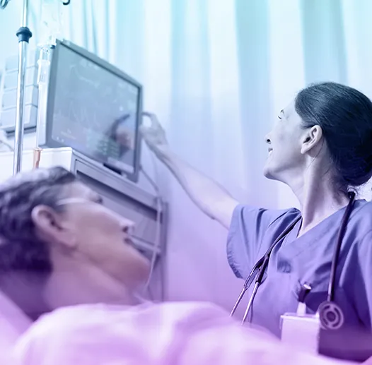 Nurse in scrubs and stethoscope checking patient vitals on a medical monitor while attending to a patient lying in a hospital bed, with soft gradient lighting.