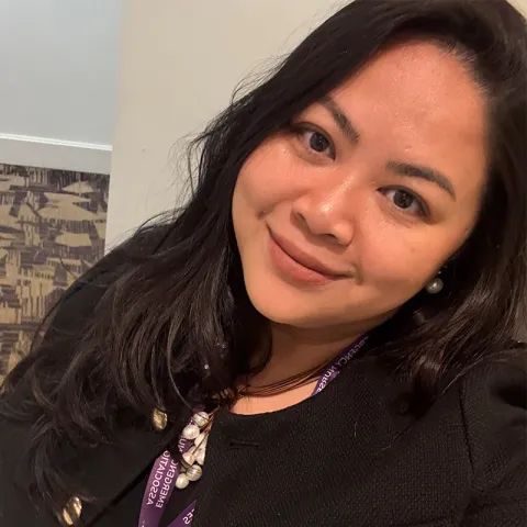 Portrait of a smiling woman wearing a black top and a purple Emergency Nurses Association lanyard, with long dark hair and pearl earrings.
